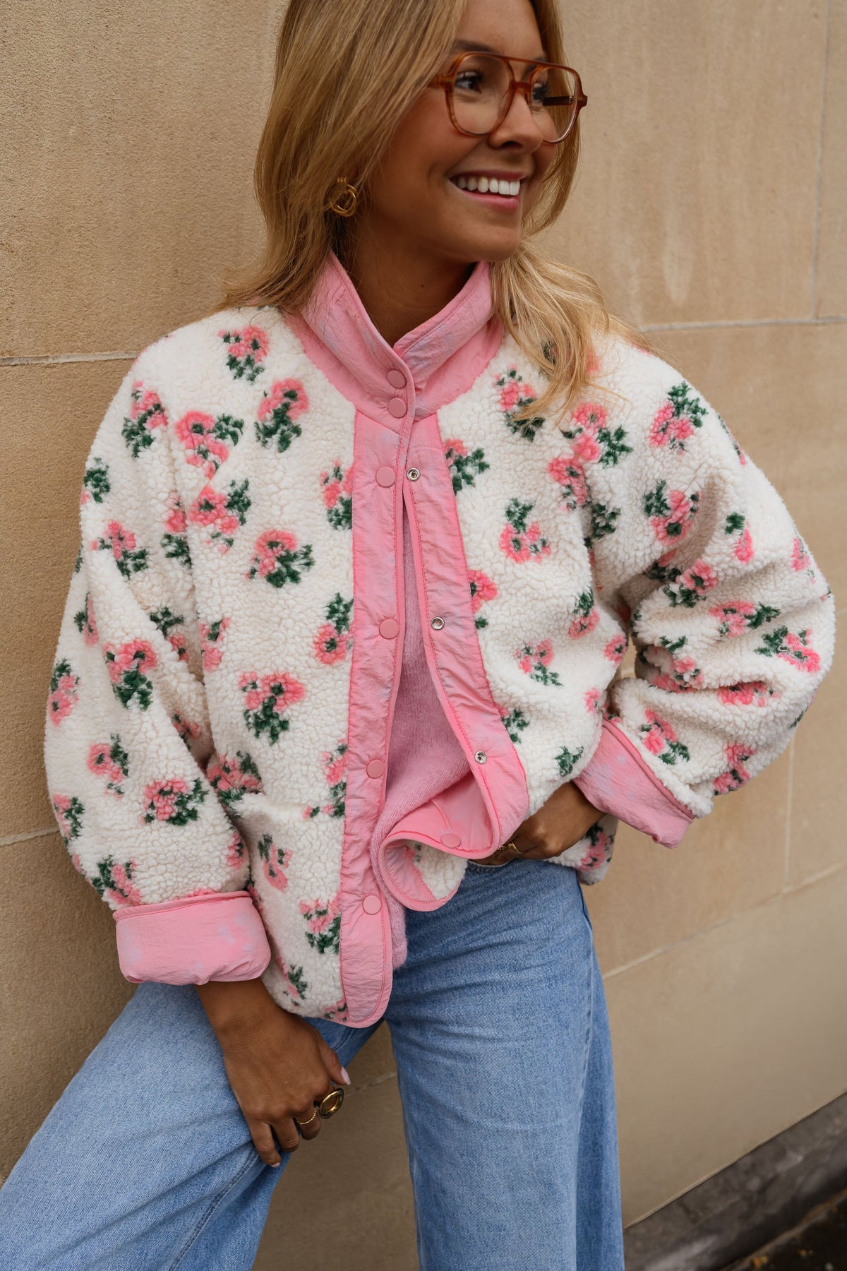 Veste polaire réversible fleurie portée par une femme, vue de face, mur beige, foulard rose