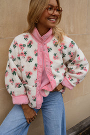 Veste polaire réversible fleurie portée par une femme, vue de face, mur beige, foulard rose