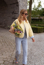 Veste matelassée à doublure rayée portée par une femme, silhouette entière, bouquet de fleurs, lunettes