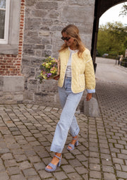 Veste matelassée à doublure rayée portée par une femme, silhouette entière, rue pavée, bouquet