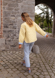 Veste matelassée à doublure rayée portée par une femme, vue de dos, rue pavée, jean