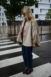 Veste souple à revers velours beige portée par une femme, vue de trois-quarts, passage piéton, jean foncé
