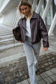 Veste souple en simili cuir bordeaux portée par une femme, en marchant, pavés, sac marron