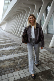 Veste souple en simili cuir bordeaux portée par une femme, vue de face, piliers blancs, jean gris