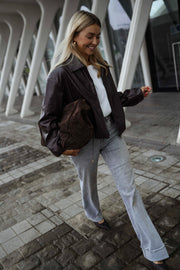Veste souple en simili cuir bordeaux portée par une femme, vue de trois-quarts, pavés, sac marron