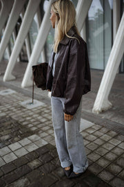 Veste souple en simili cuir bordeaux portée par une femme, vue de profil, piliers blancs, sac marron