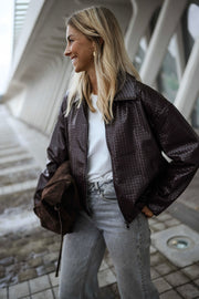 Veste souple en simili cuir bordeaux portée par une femme, vue de trois-quarts, sac marron, regard de côté