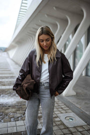 Veste souple en simili cuir bordeaux portée par une femme, vue de face, escalier, sac marron