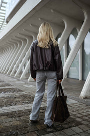 Veste souple en simili cuir bordeaux portée par une femme, vue de dos, pavés, sac noir