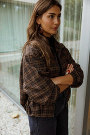 Veste à carreaux à poches portée par une femme, vue de trois-quarts, baie vitrée, bras croisés