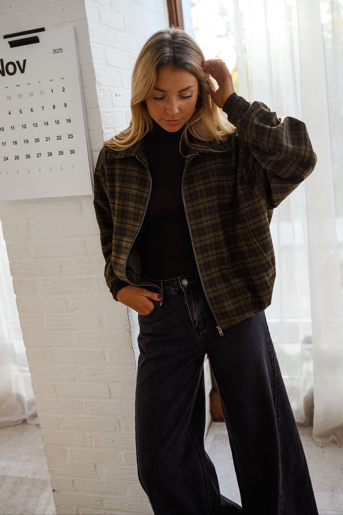 Veste à carreaux zippée portée par une femme, vue de face, mur blanc, pantalon noir