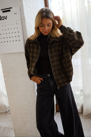 Veste à carreaux zippée portée par une femme, vue de face, mur blanc, pantalon noir