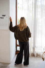 Veste à carreaux zippée portée par une femme, vue de dos, mur blanc, pantalon noir