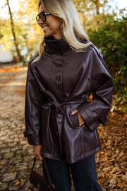 Veste en simili cuir ceinturée bordeaux portée par une femme, vue rapprochée, col relevé, lunettes de soleil