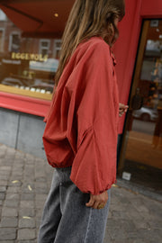 Veste courte déperlante portée par une femme, vue de dos, jean gris, vitrine rouge