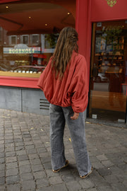 Veste courte déperlante portée par une femme, vue de dos, jean gris, devant une vitrine
