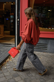 Veste courte déperlante portée par une femme, en marchant, sac rouge à la main, jean gris, trottoir