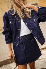 Veste en jean courte portée par une femme, vue rapprochée, couture contrastante, jupe en jean