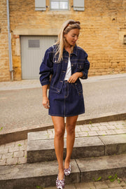 Veste en jean courte portée par une femme, vue de face, jupe en jean, marches