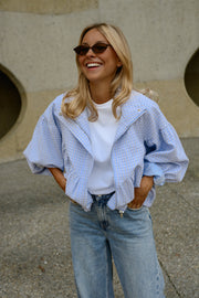 Veste à carreaux bouffante portée par une femme, vue rapprochée, lunettes de soleil, sourire, mains dans les poches