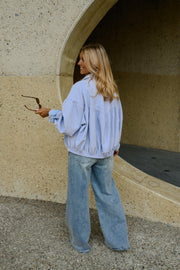 Veste à carreaux bouffante portée par une femme, silhouette entière, téléphone à la main, jean large, mur arrondi