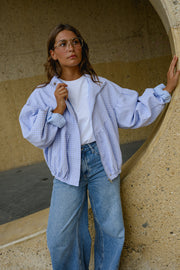 Veste à carreaux bouffante portée par une femme, silhouette entière, jean bleu, mur en pierre, veste ouverte