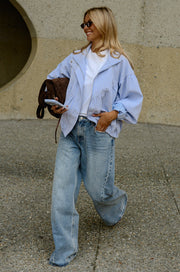 Veste à carreaux bouffante portée par une femme, en marchant, jean bleu, sac marron