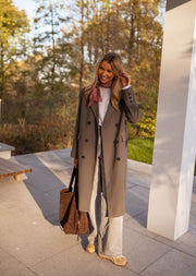 Veste longue boutonnée doublée grise portée par une femme, vue de face, sac marron, terrasse
