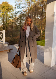 Veste longue boutonnée doublée grise portée par une femme, vue de face, sac marron, allée