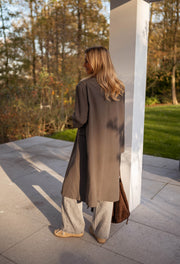 Veste longue boutonnée doublée grise portée par une femme, vue de dos, pilier, sac marron