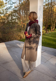 Veste longue boutonnée doublée grise portée par une femme, vue de trois-quarts, écharpe rouge, pilier