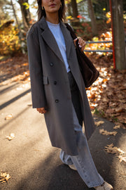 Veste longue boutonnée doublée grise portée par une femme, vue de face, feuilles d'automne, pantalon gris