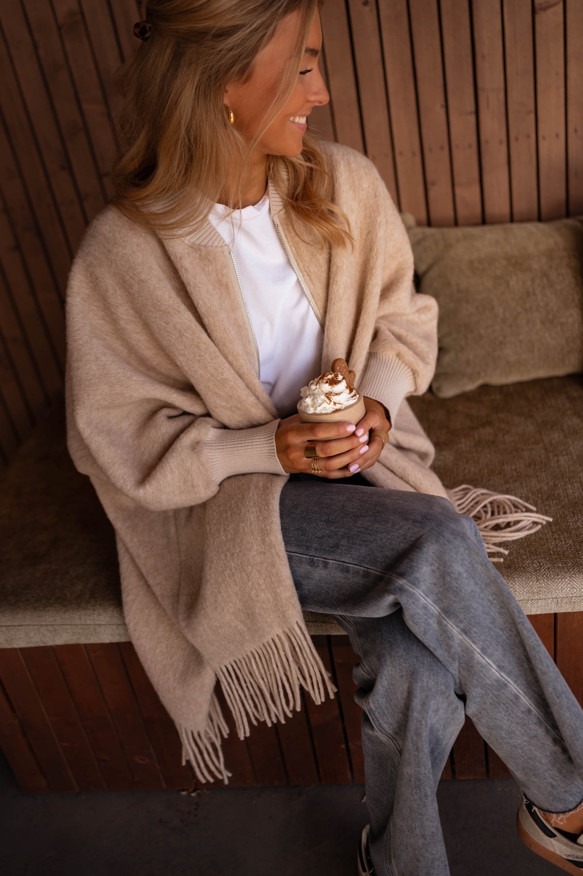 Veste ample à franges portée par une femme, assise, banc en bois, jean
