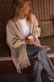 Veste ample à franges portée par une femme, assise, banc en bois, jean