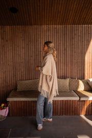 Veste ample à franges portée par une femme, vue de profil, banc en bois, jean