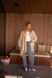 Veste ample à franges portée par une femme, silhouette entière, banc en bois, jean