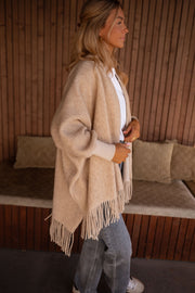 Veste ample à franges portée par une femme, vue de trois-quarts, jean, mur en bois