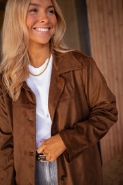 Veste effet daim ceinturée chocolat portée par une femme, vue rapprochée, sourire, haut blanc