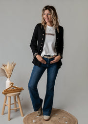 Veste officier à revers léopard portée par une femme, silhouette entière, jean flare, tabouret