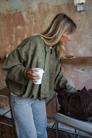 Veste loose à zip doré kaki portée par une femme, vue rapprochée, mur en briques, gobelet