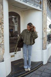 Veste loose à zip doré kaki portée par une femme, vue de face, porte vitrée, sac marron