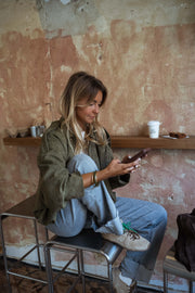 Veste loose à zip doré kaki portée par une femme, assise, tabouret, téléphone