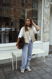 Veste sans manches à poches beige portée par une femme, vue de face, vitrine, sac marron