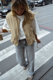 Veste sans manches à poches beige portée par une femme, vue de face, passage piéton, jean gris