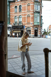 Veste sans manches à poches beige portée par une femme, vue de face, rue, immeubles en briques