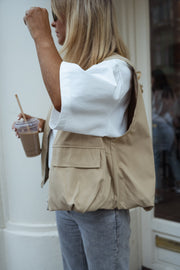 Veste sans manches à poches beige portée par une femme, vue rapprochée, t-shirt blanc, gobelet