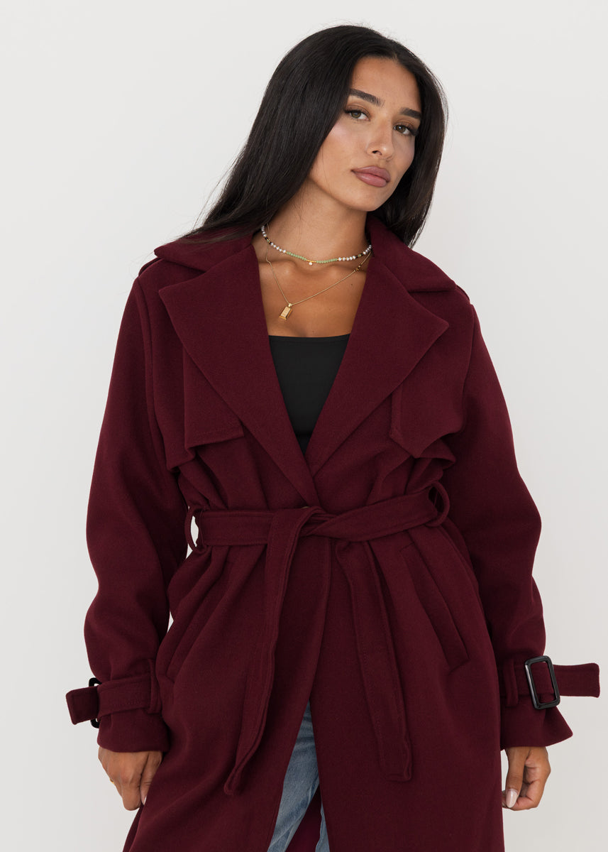 Trench oversize bordeaux à ceinture — vue portée de face, ouvert sur un haut noir et jean clair