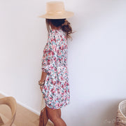 Robe fleurie à lurex portée par une femme, vue de dos, mur blanc, chapeau