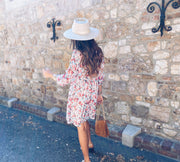 Robe fleurie à lurex portée par une femme, silhouette entière, mur en pierre, chapeau blanc