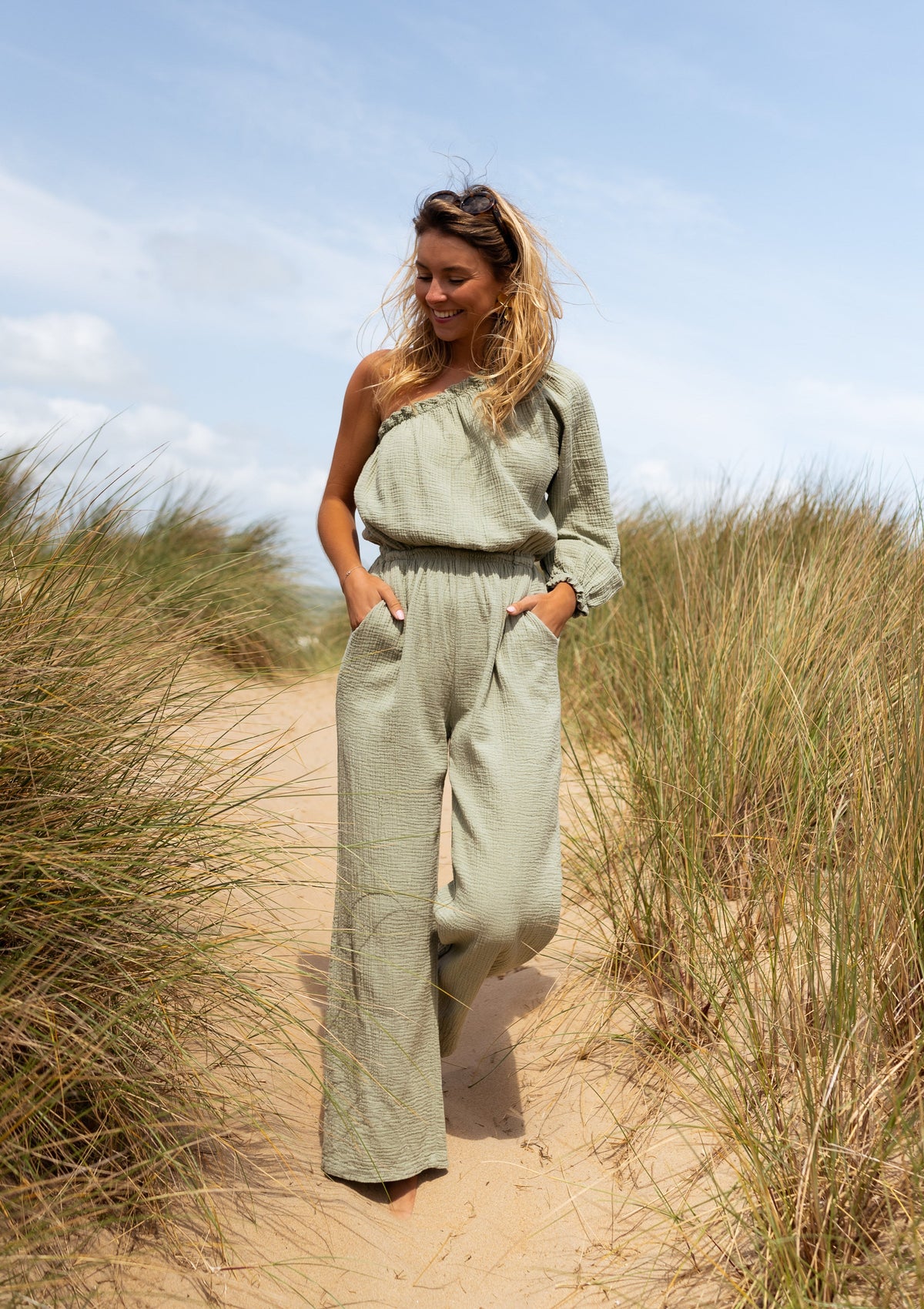 Combinaison asymétrique à poches portée par une femme, vue de face, dunes, herbes